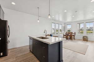 Kitchen featuring decorative light fixtures, appliances with stainless steel finishes, recessed lighting, light wood finished floors, and a kitchen island with sink