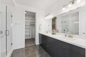Full bathroom featuring a walk in closet, a stall shower, double vanity, and dark tile patterned floors