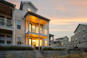 Back of property at dusk with stucco siding, a balcony, and a porch