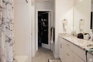 Bathroom featuring a spacious closet, double vanity, shower / tub combo with curtain, and light tile patterned floors