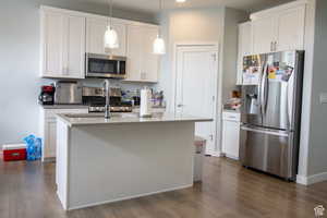 Kitchen with stainless steel appliances, white cabinets, an island with sink, dark wood-type flooring, and recessed lighting