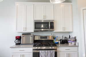 Kitchen featuring appliances with stainless steel finishes, white cabinets, and light stone countertops