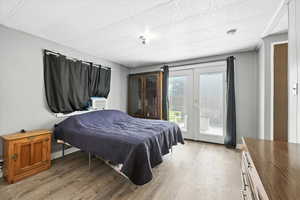 Bedroom with access to exterior, light wood-style floors, french doors, and a textured ceiling