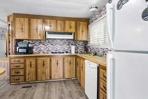 Kitchen featuring white appliances, light countertops, decorative backsplash, light wood finished floors, and brown cabinetry