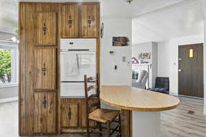 Kitchen with white oven, light wood finished floors, a warming drawer, brown cabinetry, and a breakfast bar area