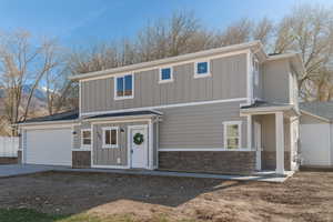 View of front of home with board and batten siding, concrete driveway, stone siding, and an attached garage
