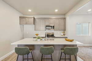 Kitchen with appliances with stainless steel finishes, light stone counters, a breakfast bar, a kitchen island with sink, and recessed lighting