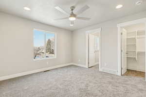 Unfurnished bedroom with a spacious closet, light colored carpet, a textured ceiling, ceiling fan, and recessed lighting