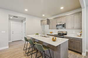 Kitchen with appliances with stainless steel finishes, light wood-style flooring, a breakfast bar, light stone countertops, and recessed lighting