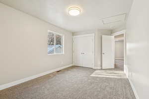 Unfurnished bedroom featuring attic access, carpet flooring, a textured ceiling, and a closet