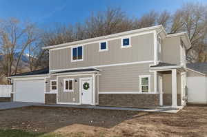 View of front of property featuring stone siding, concrete driveway, an attached garage, and board and batten siding