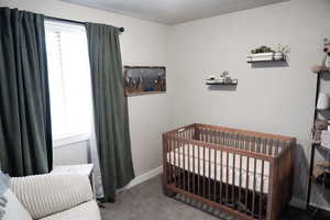 Carpeted bedroom featuring baseboards and a nursery area