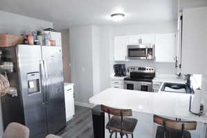 Kitchen with stainless steel appliances, white cabinetry, a peninsula, dark wood-style flooring, and a textured ceiling