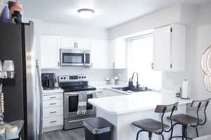 Kitchen featuring appliances with stainless steel finishes, light countertops, a peninsula, a breakfast bar area, and white cabinetry