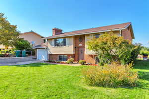 Split foyer home featuring brick siding, a front yard, a chimney, and driveway