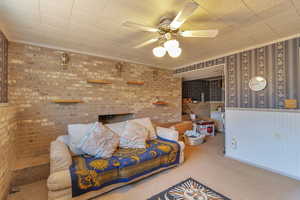 Living room featuring carpet, a ceiling fan, wallpapered walls, and brick wall