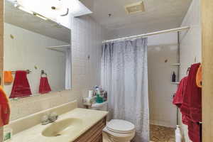 Bathroom featuring a tile shower, tile walls, vanity, and a textured ceiling