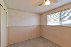 Empty room featuring a ceiling fan, carpet floors, wallpapered walls, and wainscoting