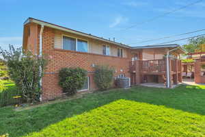 Back of property with brick siding, a yard, and a wooden deck