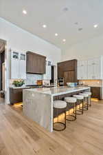 Kitchen featuring tasteful backsplash, white cabinets, light stone counters, dark brown cabinets, and a kitchen bar