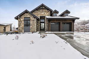 View of front of home with stone siding, an attached garage, and driveway