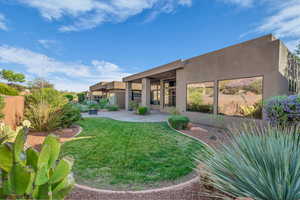 Rear view of house with stucco siding, a patio area, and a lawn