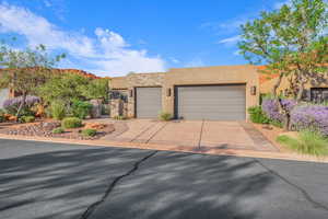 Adobe home with stone siding, stucco siding, concrete driveway, a garage, and a gate