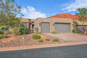 Pueblo revival-style home with stucco siding, concrete driveway, stone siding, and an attached garage