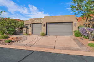 Pueblo-style home featuring stucco siding, stone siding, driveway, a garage, and a gate