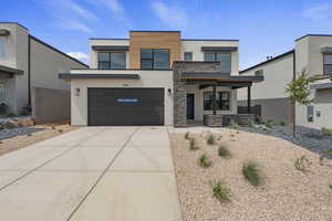 Modern home with stone siding, concrete driveway, stucco siding, a garage, and a porch