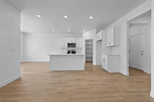 Kitchen with light countertops, white cabinetry, an island with sink, recessed lighting, and light wood finished floors