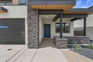 Doorway to property with stone siding, covered porch, stucco siding, and a garage