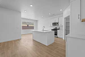 Kitchen with an island with sink, stainless steel appliances, white cabinetry, light wood-style flooring, and recessed lighting