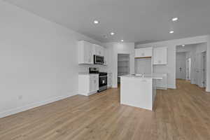 Kitchen with white cabinets, stainless steel appliances, an island with sink, recessed lighting, and light wood-style floors