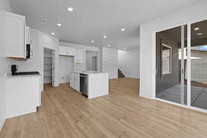Kitchen with recessed lighting, a center island with sink, open floor plan, light wood finished floors, and white cabinetry