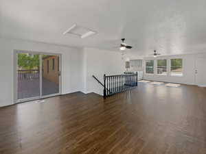 Unfurnished living room featuring attic access, dark wood-type flooring, ceiling fan, and a textured ceiling