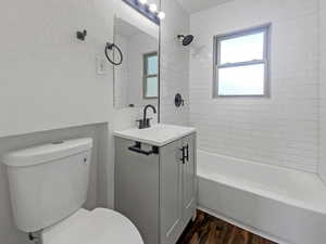 Full bathroom with a textured wall, shower / bath combination, vanity, and dark wood-style flooring