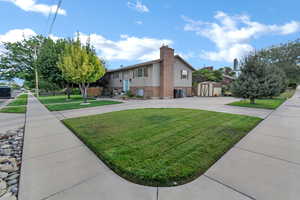 View of property exterior featuring a storage unit, a yard, a chimney, brick siding, and driveway