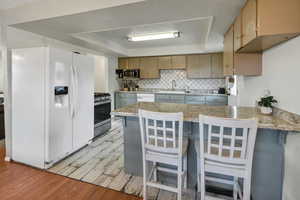 Kitchen with a peninsula, appliances with stainless steel finishes, a raised ceiling, light wood finished floors, and a breakfast bar