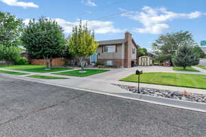 View of front of property with a front lawn, a storage unit, concrete driveway, a chimney, and brick siding
