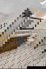 Full bathroom featuring tile walls, vanity, light tile patterned floors, a textured ceiling, and wainscoting