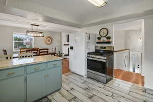 Kitchen with stainless steel range with gas cooktop, light wood finished floors, pendant lighting, and light stone countertops