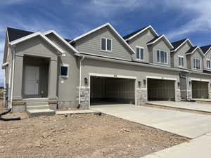 View of front of property with driveway, stone siding, stucco siding, and a garage