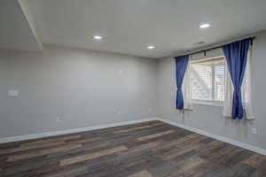 Empty room featuring a textured ceiling, recessed lighting, and dark wood-style flooring