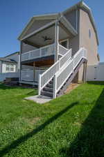Rear view of property with ceiling fan, stairway, a lawn, and stucco siding