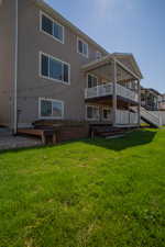 Rear view of house featuring a deck, stucco siding, and a lawn