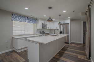 Kitchen featuring appliances with stainless steel finishes, white cabinetry, hanging light fixtures, tasteful backsplash, and an island with sink