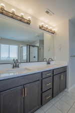 Full bath featuring double vanity, light tile patterned floors, and a stall shower