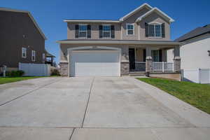 View of front facade featuring stone siding, covered porch, concrete driveway, stucco siding, and a garage