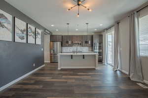 Kitchen with backsplash, a center island with sink, stainless steel appliances, dark wood-style floors, and decorative light fixtures
